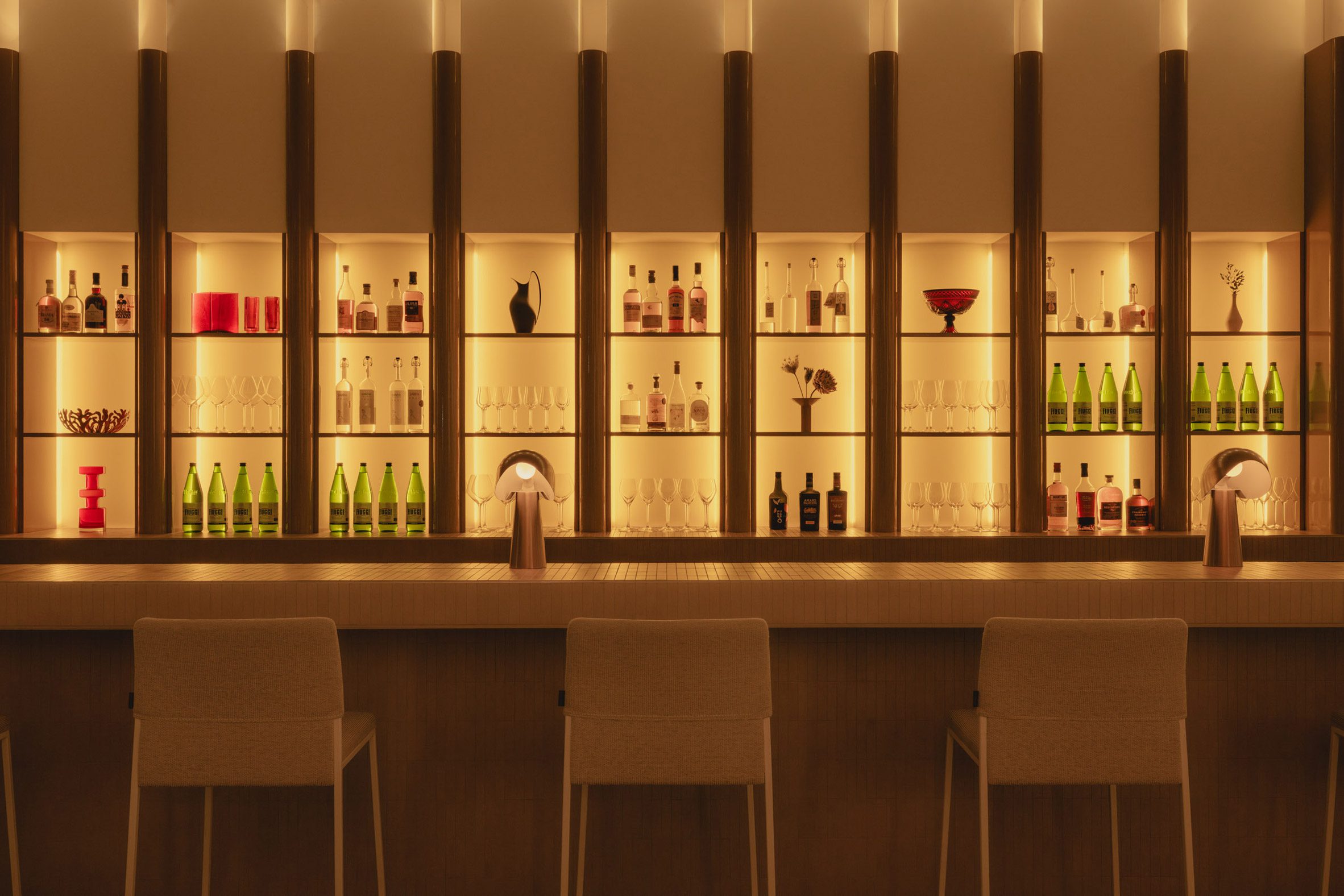 Fluted glass divides a grid of glowing niches behind a bar